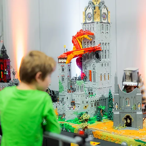 Een jongen bekijkt een LEGO® kasteel met een rode draak op de toren