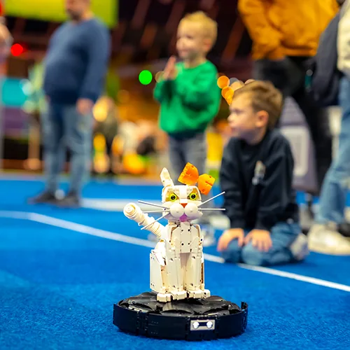 Een witte LEGO® kat op een draaiend platform, met spelende kinderen erachter