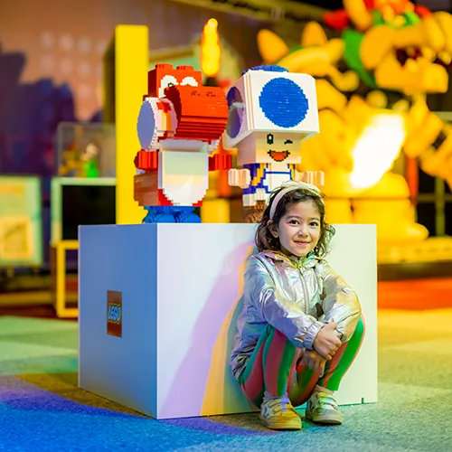 Een meisje zit voor twee LEGO® figuren uit Super Mario