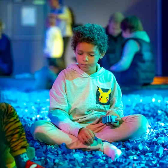 Een kind zit in een bak vol blauwe LEGO stenen