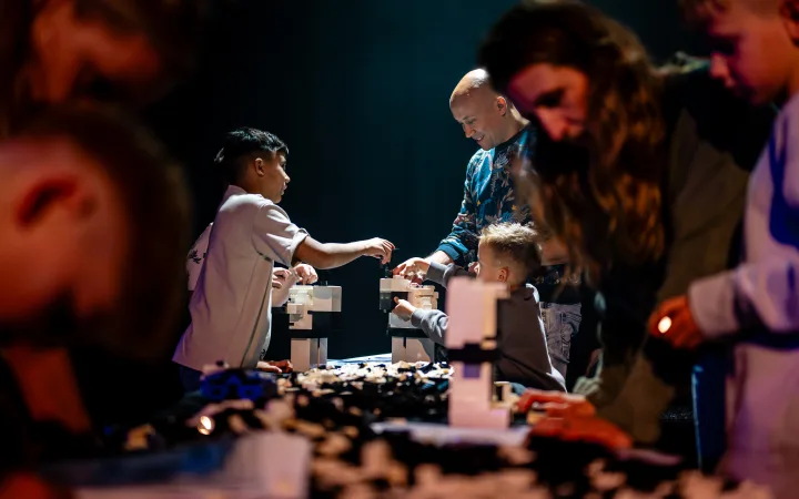Een groep kinderen bouwt samen aan modellen op een verlicht podium.