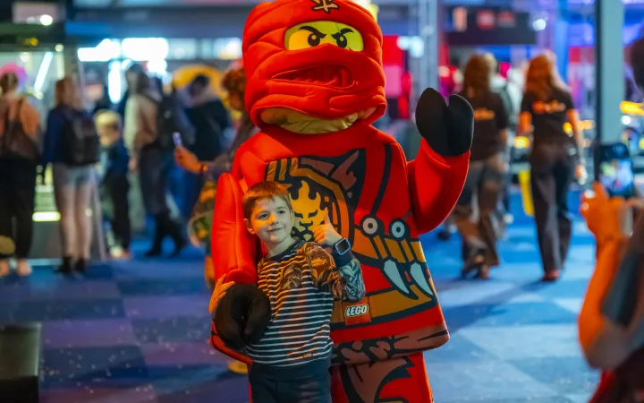 Een jongen poseert naast de kostuummascotte van Kai uit LEGO NINJAGO.