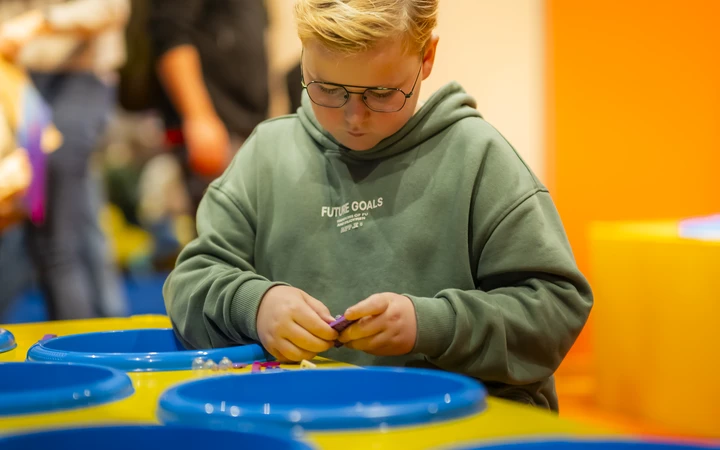 Een jongen stelt zijn eigen minifiguur samen aan een tafel met onderdelenbakjes.